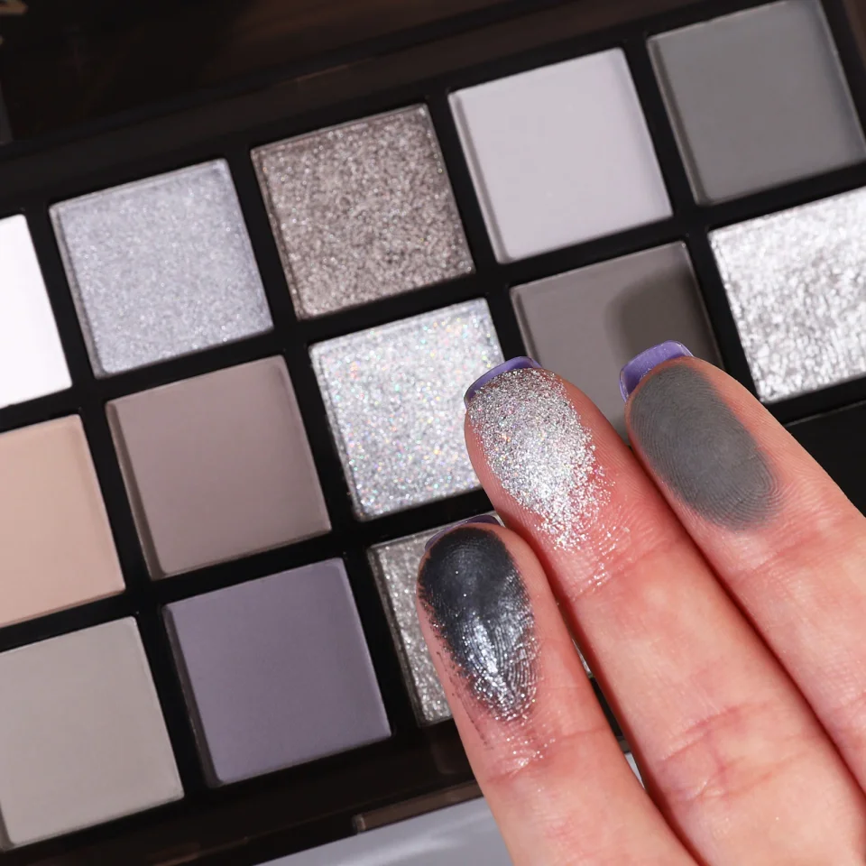 UCANBE Black Meteors eyeshadow palette swatches on fingers showing silver and grey shades